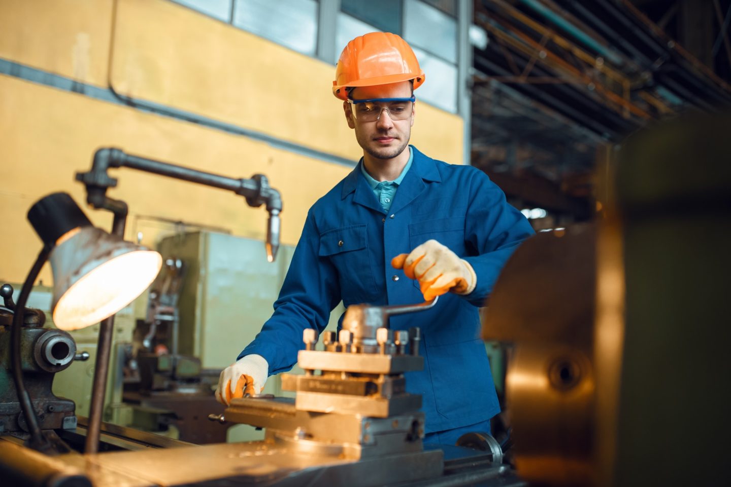 Worker in uniform and helmet works on lathe